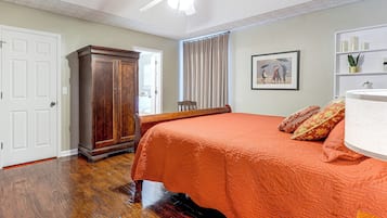 A bedroom with a wooden wardrobe, a bed with an orange bedspread, a ceiling fan, and a framed picture on the wall.