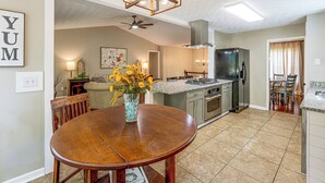 A kitchen with a central island, a dining table with chairs, a ceiling fan, and a refrigerator.