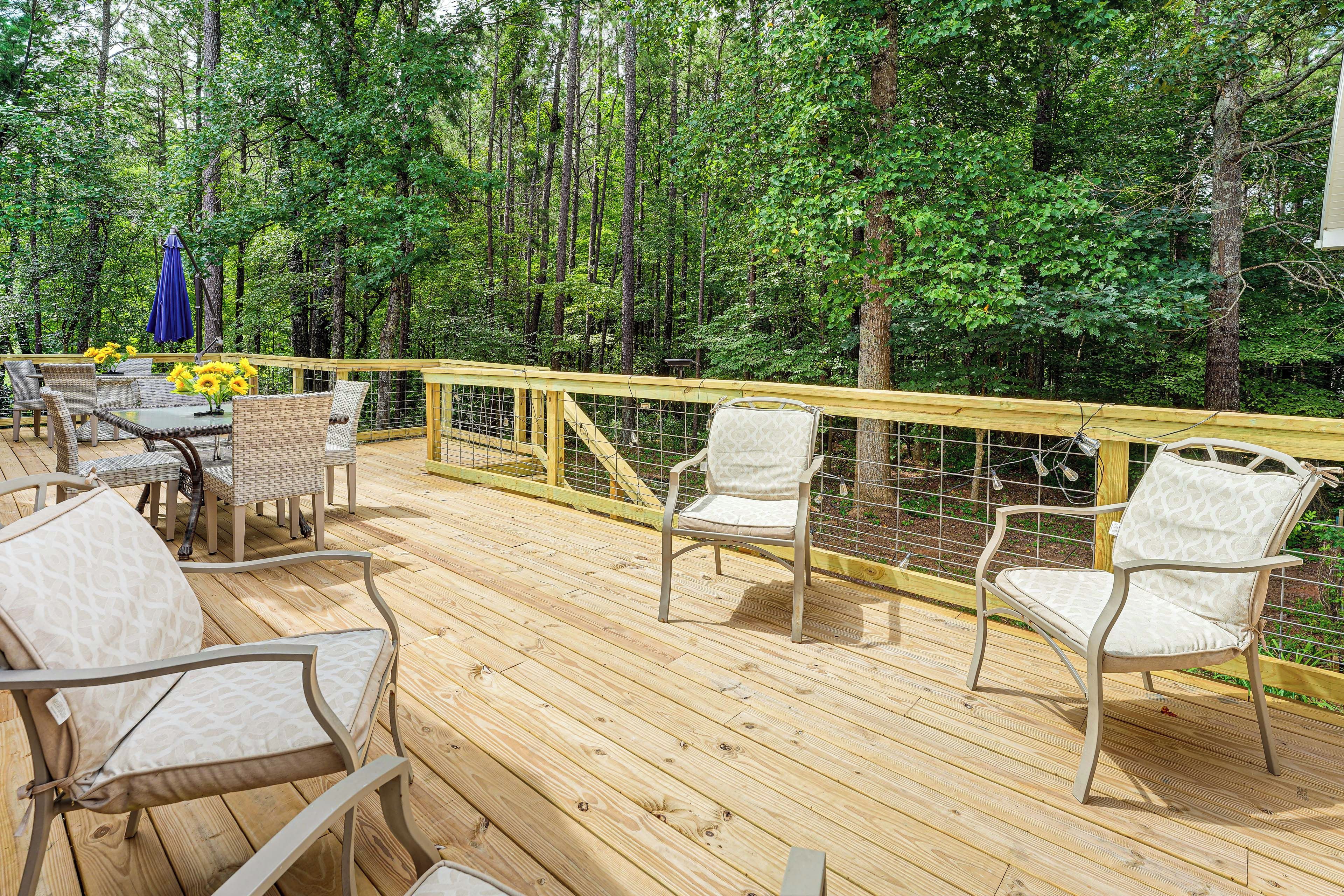 A wooden deck with outdoor furniture, surrounded by a wooden railing, set in a forested area.