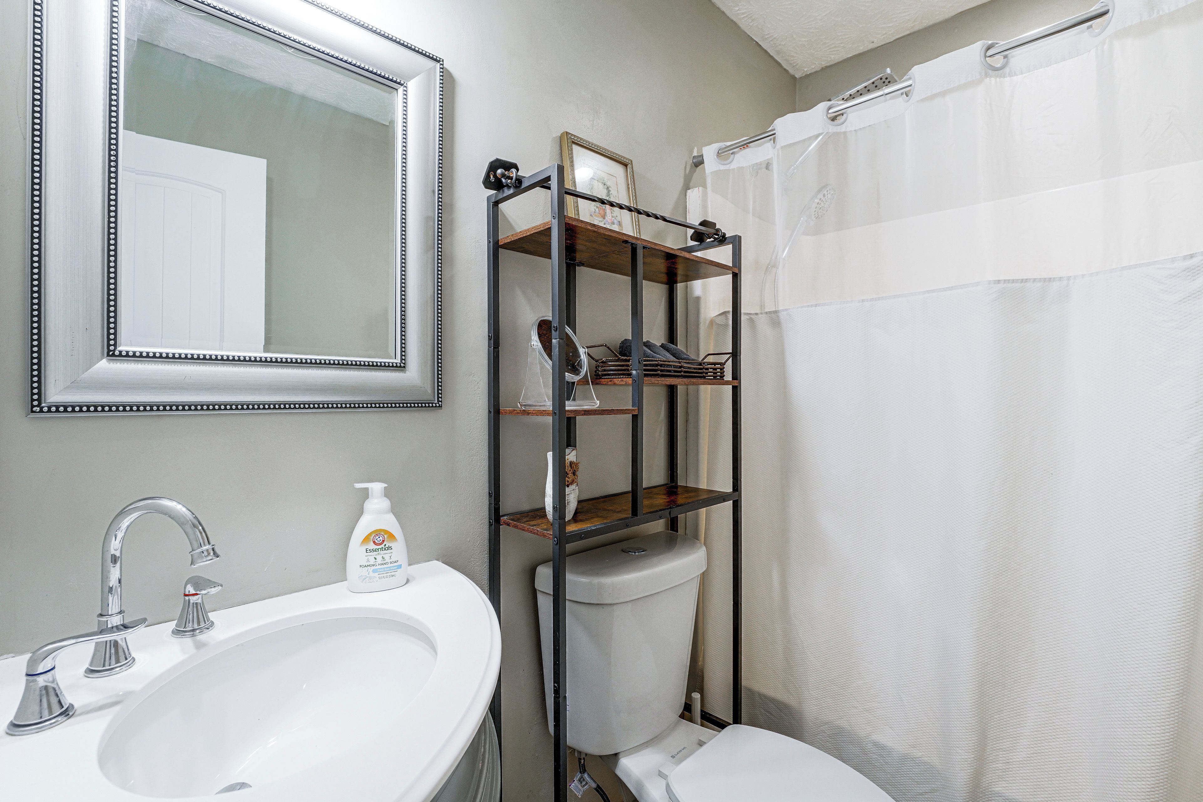 A bathroom with a white sink, a mirror, a toilet, and a shower curtain.