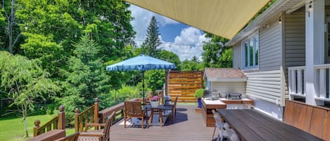 An outdoor deck with wooden furniture, a barbecue area, and a covered seating area with a blue umbrella.