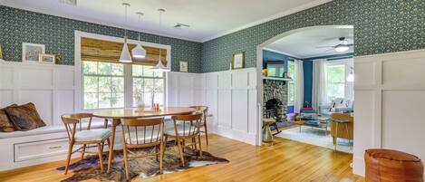 A room with a wooden dining table, chairs, a white sofa, and a stone fireplace.