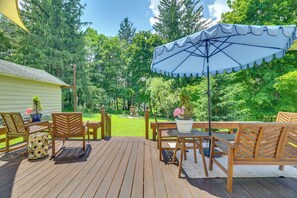 A wooden deck with outdoor furniture, a covered area with an umbrella, and a view of a green landscape with trees. - Family-friendly Poconos Getaway 11 Mi to Kalahari! (Mountainhome)
