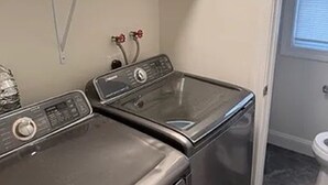 A laundry room with two stacked washers and dryers, a water heater, and a window with blinds. - Available 9/10 - 5/31/27 Coastal living, steps from the beach, 3-bedroom, (Sea Bright)