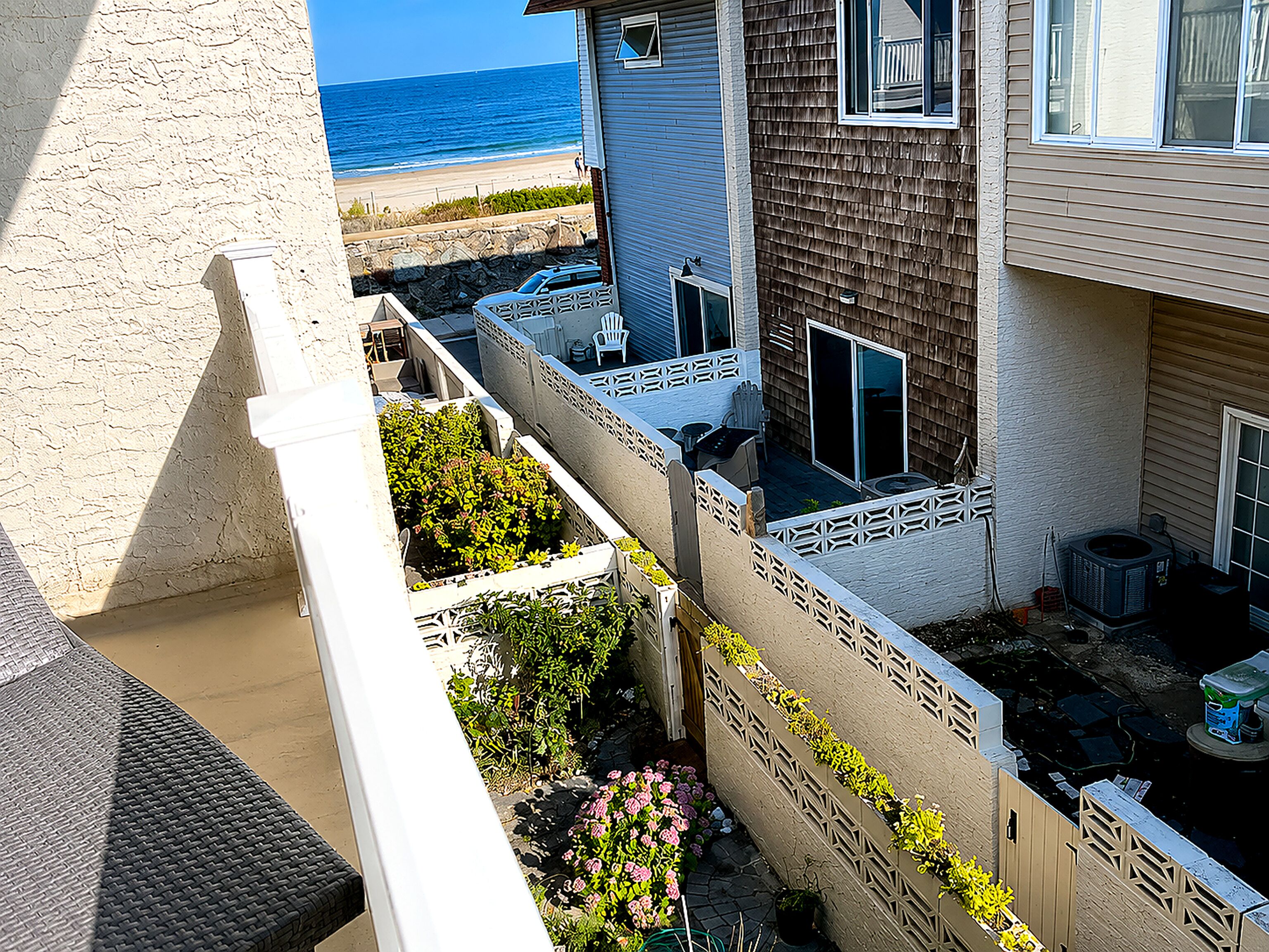 A residential building with a view of the beach, a fenced patio area with outdoor furniture, and a vehicle parked in front.