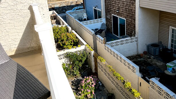 A residential building with a view of the beach, a fenced patio area with outdoor furniture, and a vehicle parked in front. - Available 9/10 - 5/31/27 Coastal living, steps from the beach, 3-bedroom, (Sea Bright)