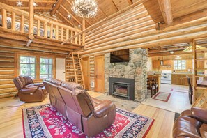 A log cabin interior with a fireplace, leather seating, and a stone wall.