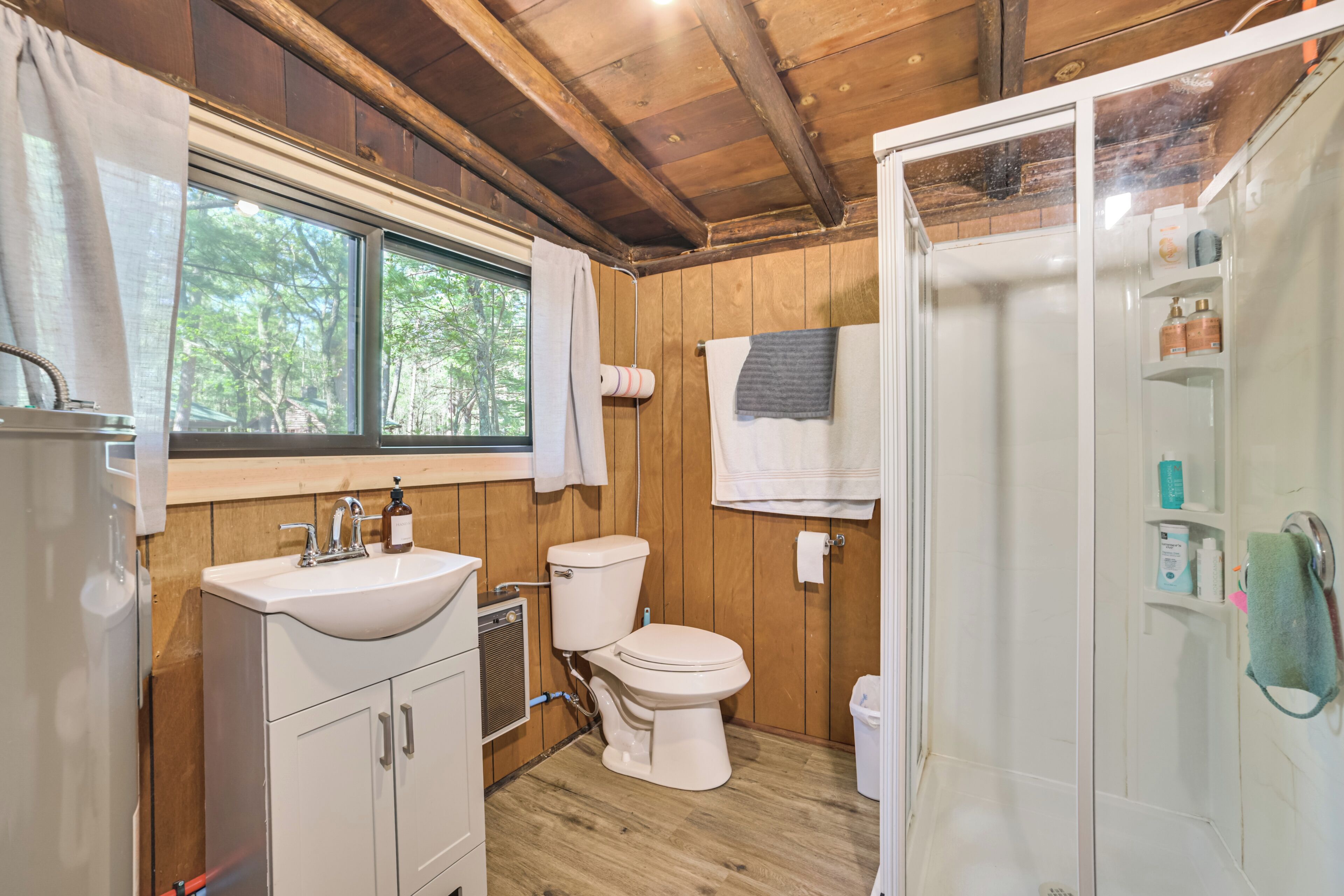 A bathroom with wooden walls, a sink, toilet, and a shower.