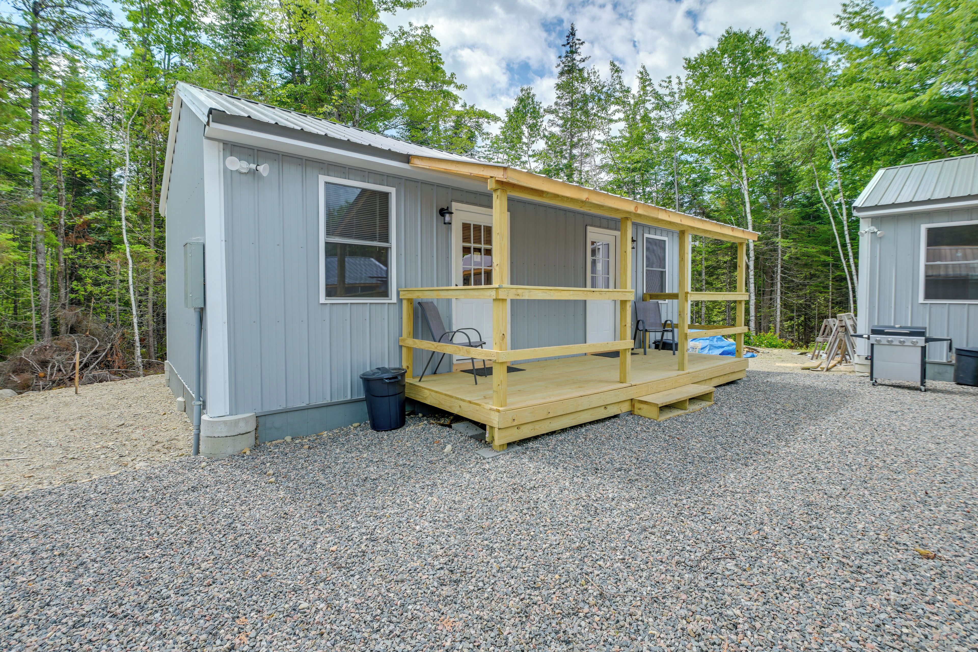A small, single-story cabin with a porch, a grill, and a gravel driveway.