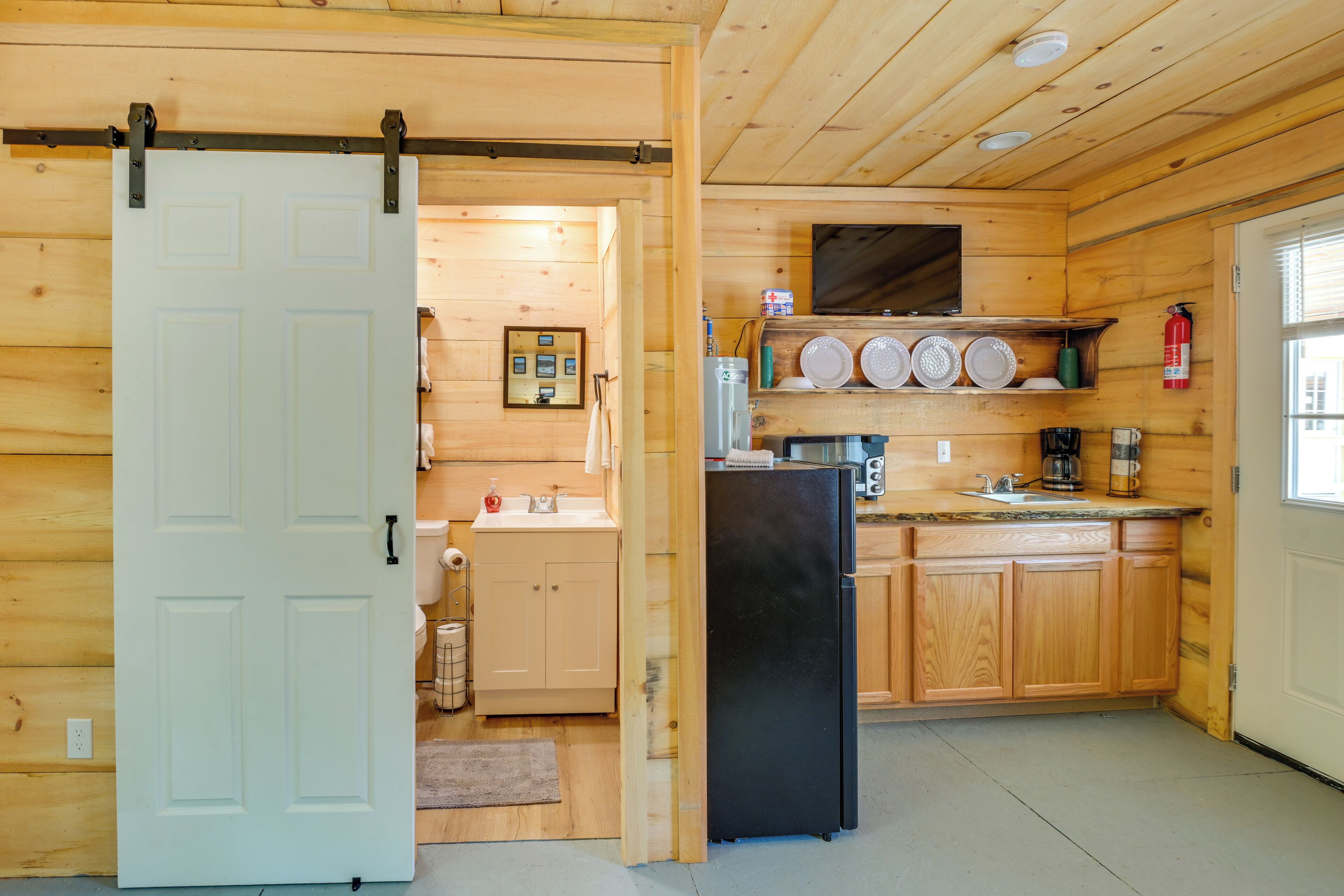 Eine kompakte Küche mit Holzschränken, einem schwarzen Kühlschrank und einem kleinen Spülbecken.