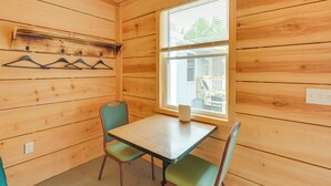 Una habitación con paneles de madera, una mesa y dos sillas, una ventana con persianas y un perchero con ganchos.
