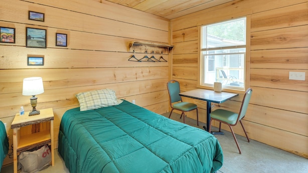 Habitación de cabaña de madera con cama, escritorio, silla y ventana.