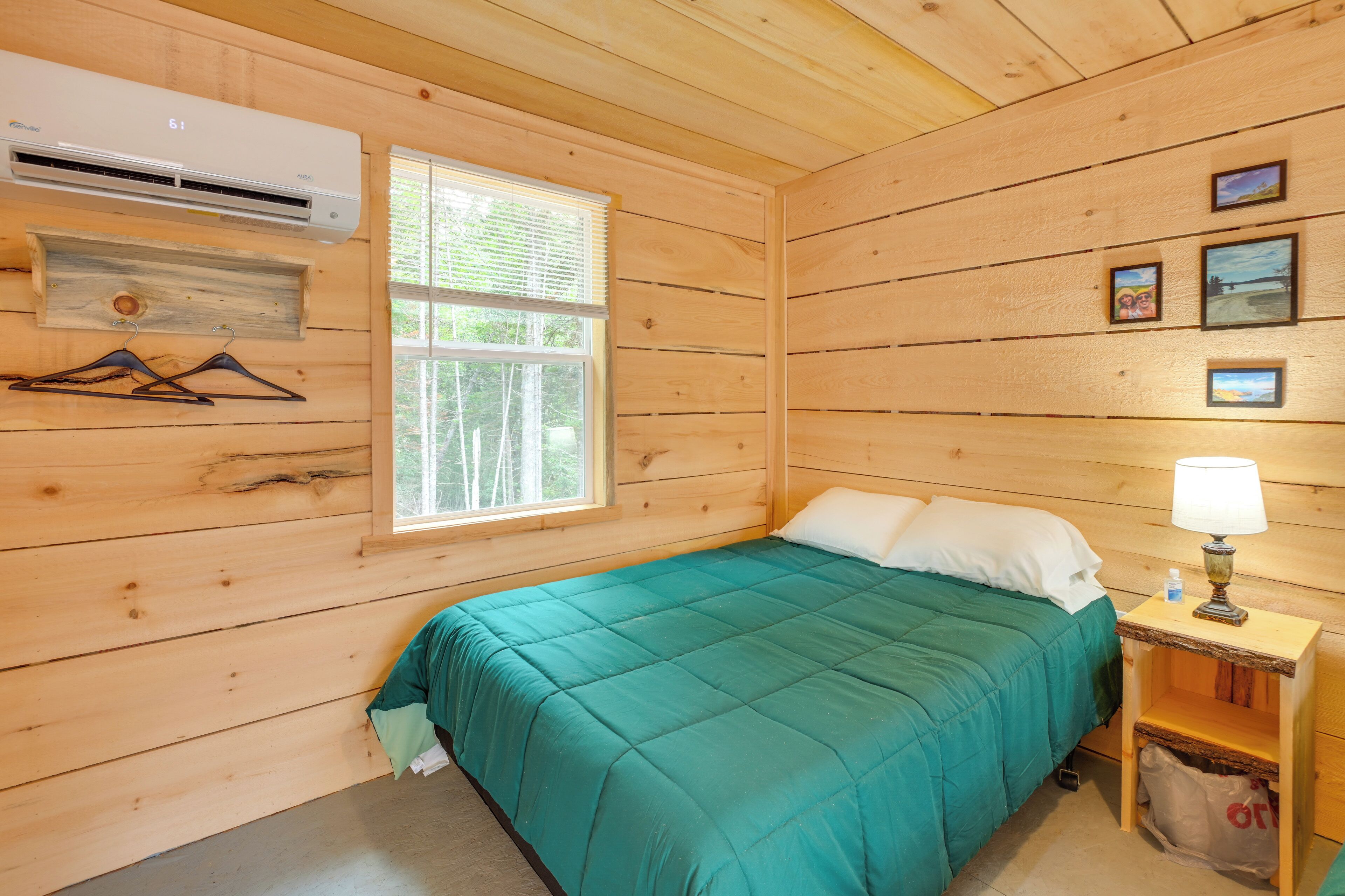 A wooden cabin room with a bed, a nightstand, a lamp, and a wall-mounted air conditioner.