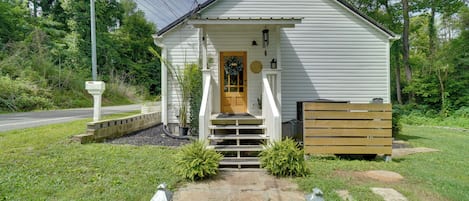A small white building with a front porch, a wooden bench, and a stone pathway leading to the entrance.