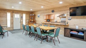 A cabin-style room with a wooden interior, a dining table with chairs, a kitchenette, and a flat-screen TV mounted on the wall. - Maine Lodge Base Camp for Hiking, Riding & Fishing (Wesley)
