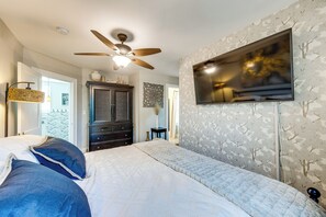 Un dormitorio con una cama, ventilador de techo, televisor montado en la pared y papel tapiz estampado.