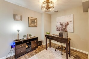Una habitación con un escritorio, una lámpara, un cuadro enmarco, un cuadro colgado en la pared y una lámpara en el techo.