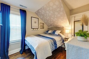 Quarto com cama, mesa de cabeceira, abajur, planta em vaso e janela com cortinas.