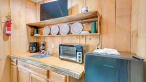 A compact kitchen with a sink, a toaster, a refrigerator, and a shelf with plates. - Ride ATV Trails! Downeast Studio for Adventurers (Wesley)