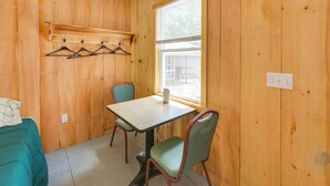 A small room with wooden walls, a table, two chairs, a coat rack with hangers, and a window with blinds. - Ride ATV Trails! Downeast Studio for Adventurers (Wesley)