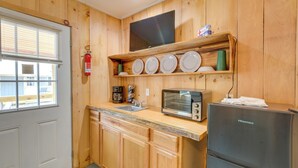 A compact kitchen with wooden cabinets, a built-in microwave, a toaster, and a small refrigerator. - Ride ATV Trails! Downeast Studio for Adventurers (Wesley)