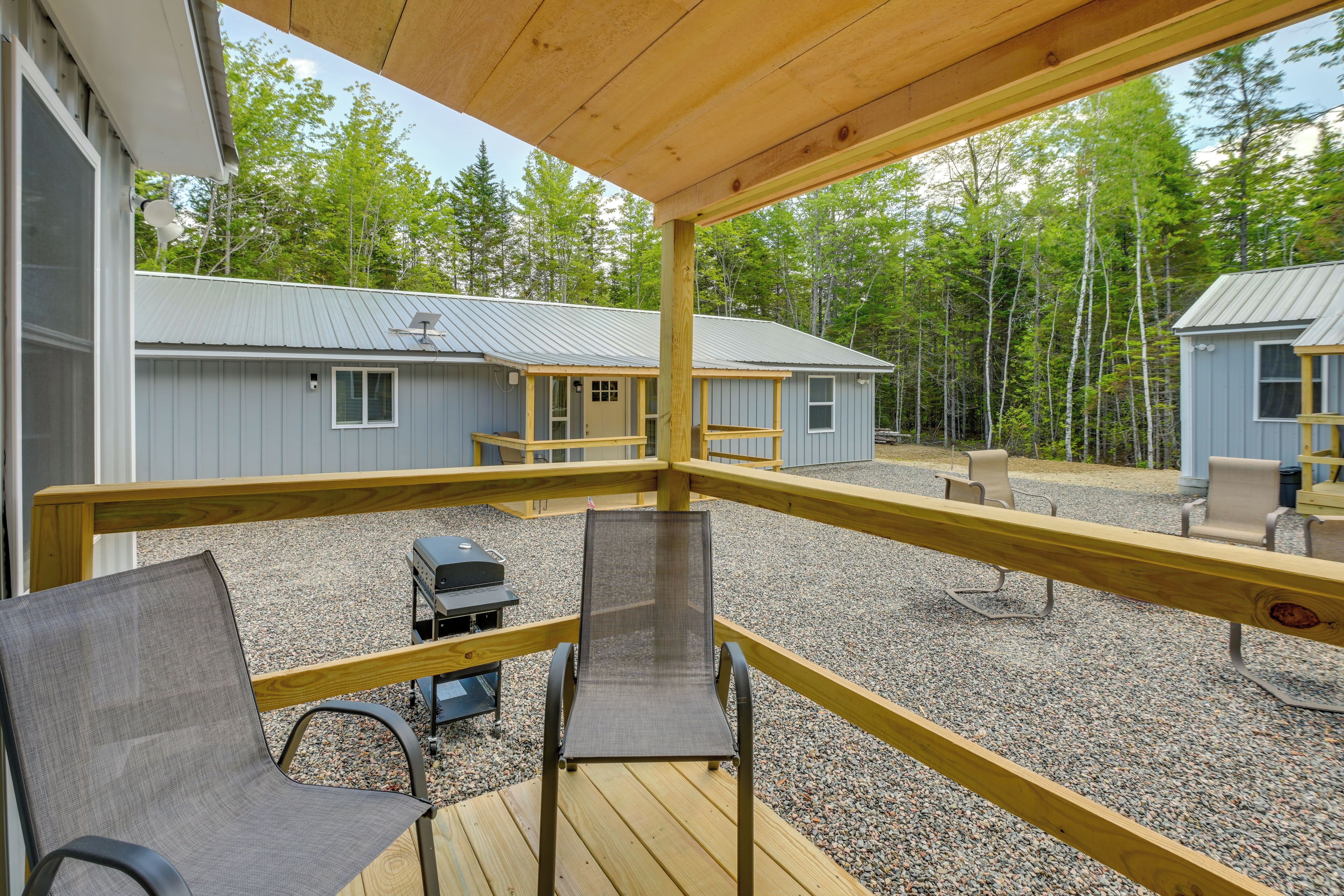 A covered outdoor deck with a grill and seating area, overlooking cabins and a forested area.