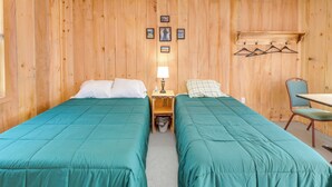 A room with two single beds, a small table with a lamp, a chair, and a coat rack with hangers. - Ride ATV Trails! Downeast Studio for Adventurers (Wesley)