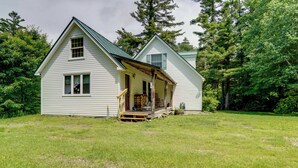 A two-story white house with a porch, surrounded by a grassy yard and trees. - Deck & Wooded Views! Rural Windham Group Retreat (West Townshend)