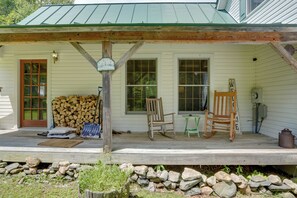 A wooden porch with a covered area, a stack of firewood, two rocking chairs, and a rustic mailbox.