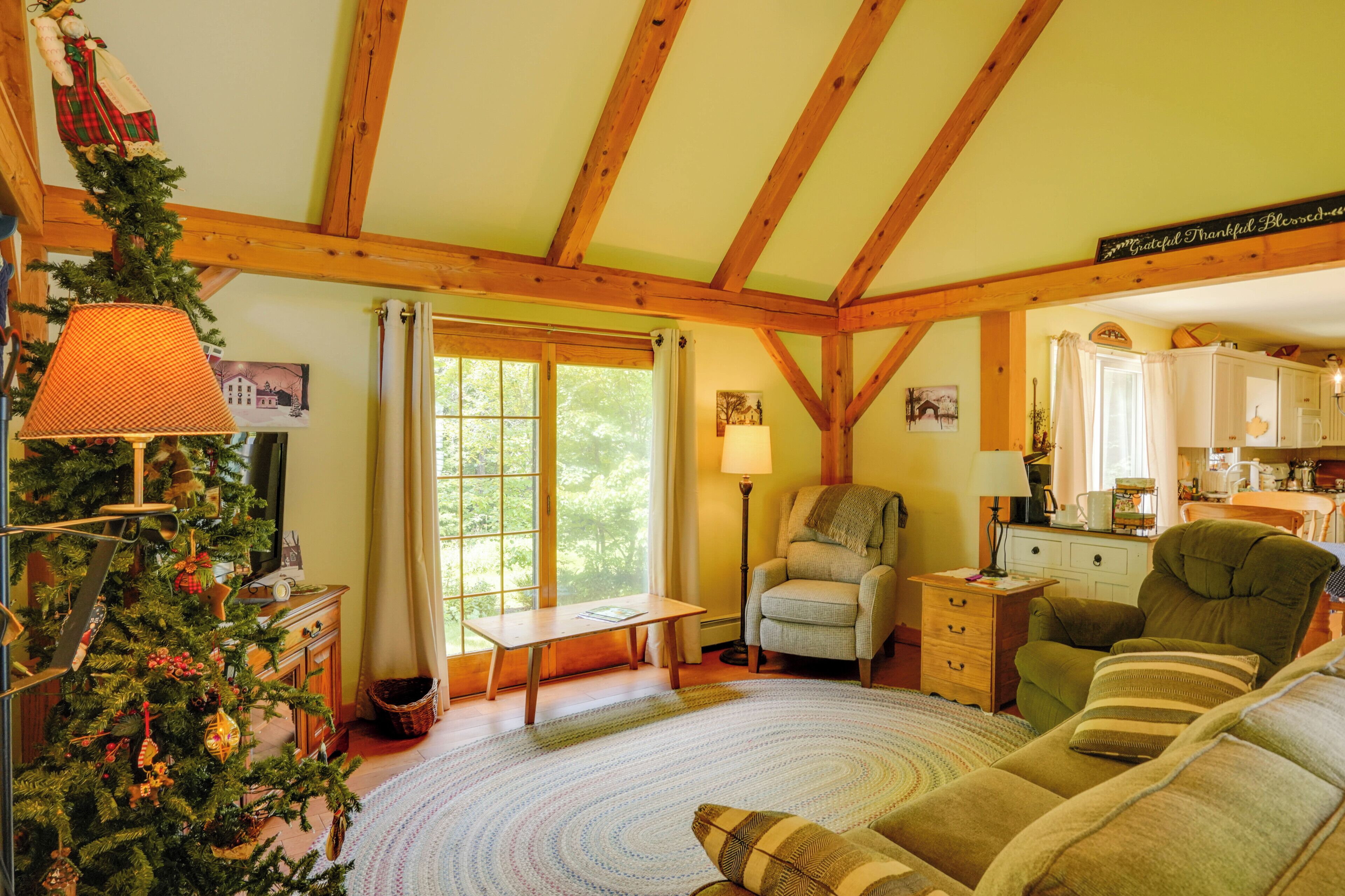 A cozy living room with a wooden ceiling, a Christmas tree, a fireplace, and a view of the outdoors.