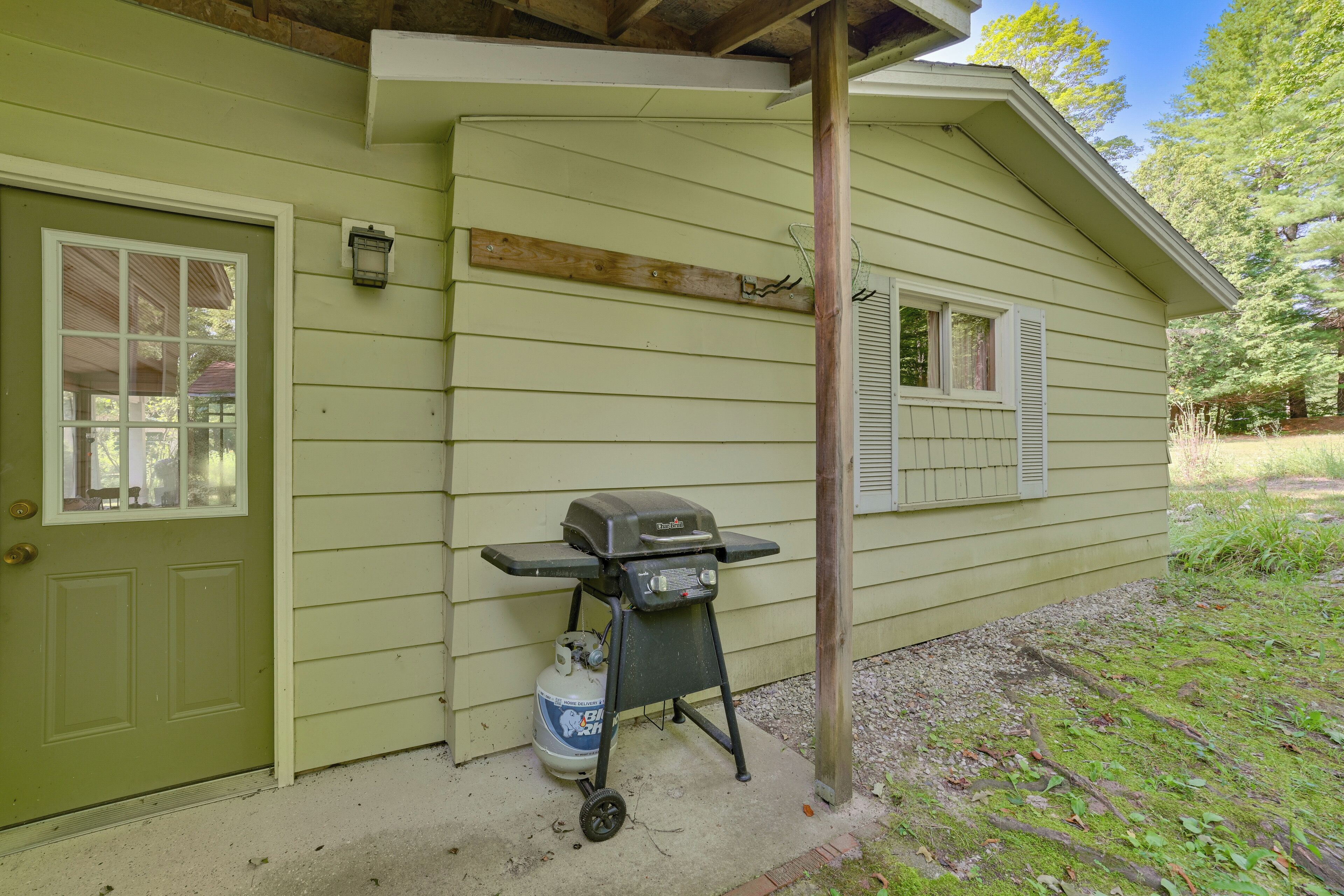 A green house with a barbecue grill and propane tank outside.