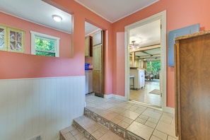 A hallway with a pink wall, white baseboard, and a tiled floor leading to a kitchen area. - Boating, Bonfires & Lake Views! Michigan Getaway (Ellsworth)