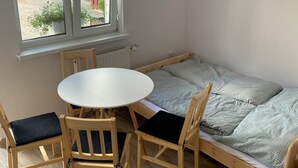 A room with a small round table and two chairs, a single bed with patterned bedding, and a window with a view of greenery. - Comfortable 4-person Room With Kitchenette (Mielno)