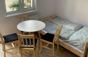 A room with a small round table and two chairs, a single bed with patterned bedding, and a window with a view of greenery. - Comfortable 4-person Room With Kitchenette (Mielno)