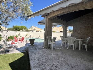 A covered outdoor area with a pool, seating, and a stone wall. - Villa des Amandiers - Premier Concierge Service (Lattes)