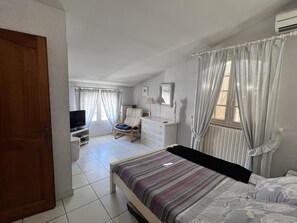 A bedroom with a bed, a chair, a dresser, a television, and a window with curtains. - Villa des Amandiers - Premier Concierge Service (Lattes)