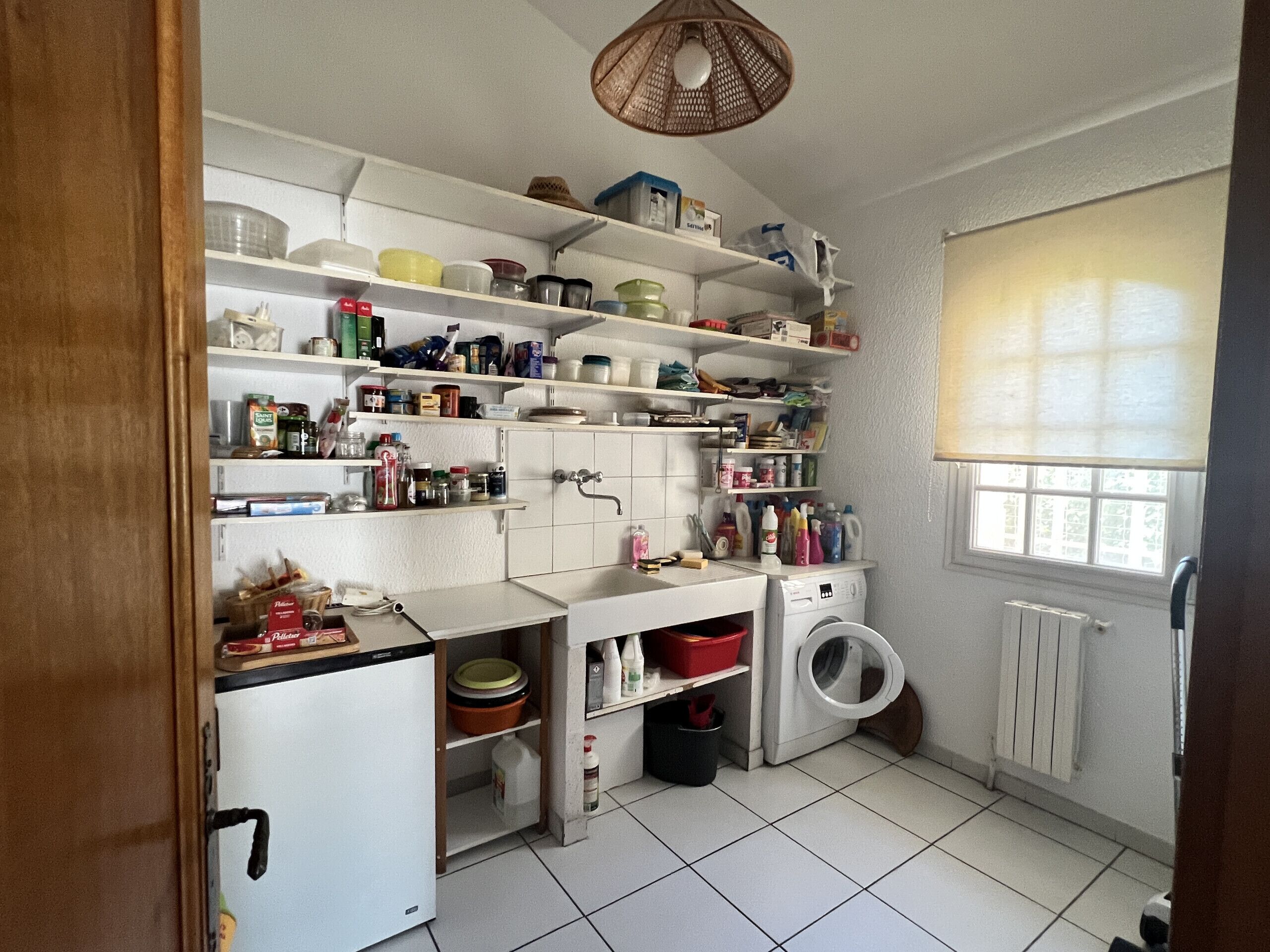 A compact kitchen with white cabinets, a built-in washing machine, and a window with blinds.