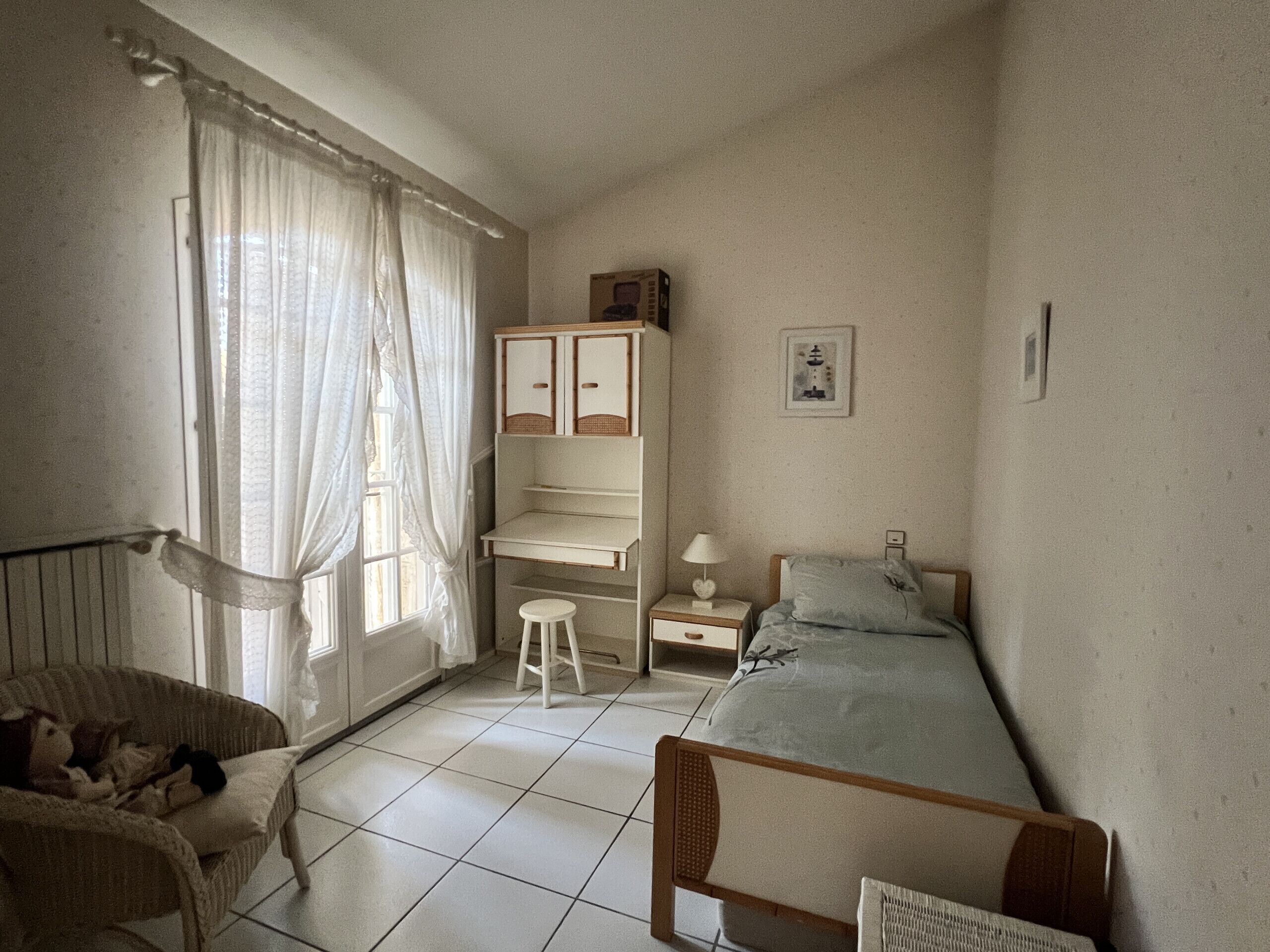 A bedroom with a bed, a desk, a chair, and a window with curtains.