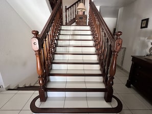 Eine Holztreppe mit Handlauf, die zu einer Zwischenebene mit einer Lampe und einem gerahmten Bild führt.
