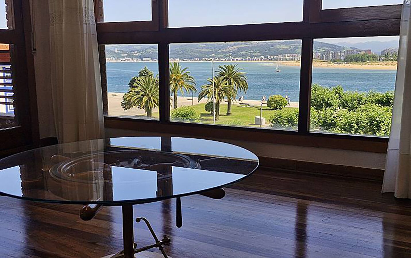 Una habitación con una mesa de vidrio y vista a una playa y al agua.