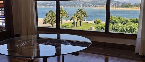 Una habitación con una mesa de vidrio y vista a una playa y al agua.
