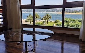 A room with a glass table and a view of a beach and water.