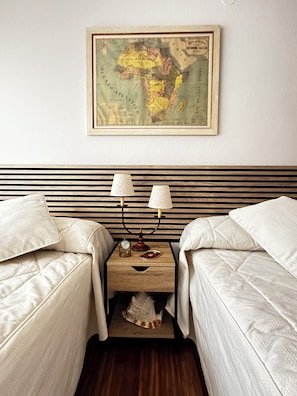 A hotel room with two beds, a wooden headboard, a nightstand with a lamp, and a framed map on the wall.