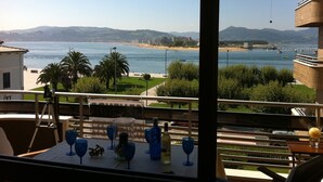 A table with wine glasses and bottles, overlooking a beach and sea.