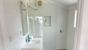 A bathroom with a white sink, a mirror, a shower, and a tiled floor. - Coastal Retreat, 2 Bedroom Apartment Near Tathra Beach (Tathra)