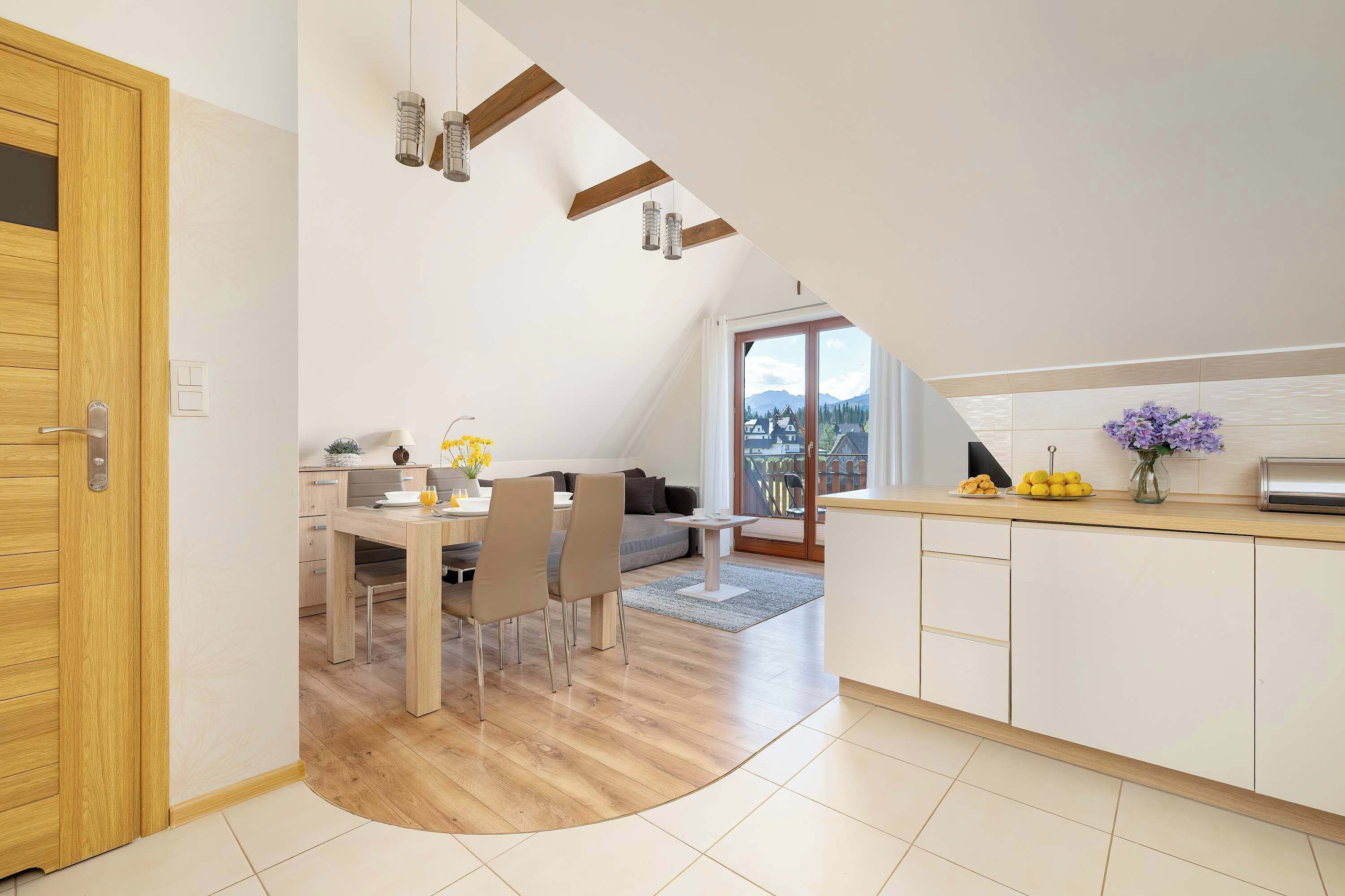 Eine moderne Küche mit Holzausstattung, ein Essbereich mit Tisch und Stühlen und Blick auf Berge durch ein großes Fenster.