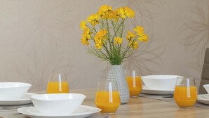 Ein Esstisch mit Tellern, Gläsern und einer Vase mit gelben Blumen.