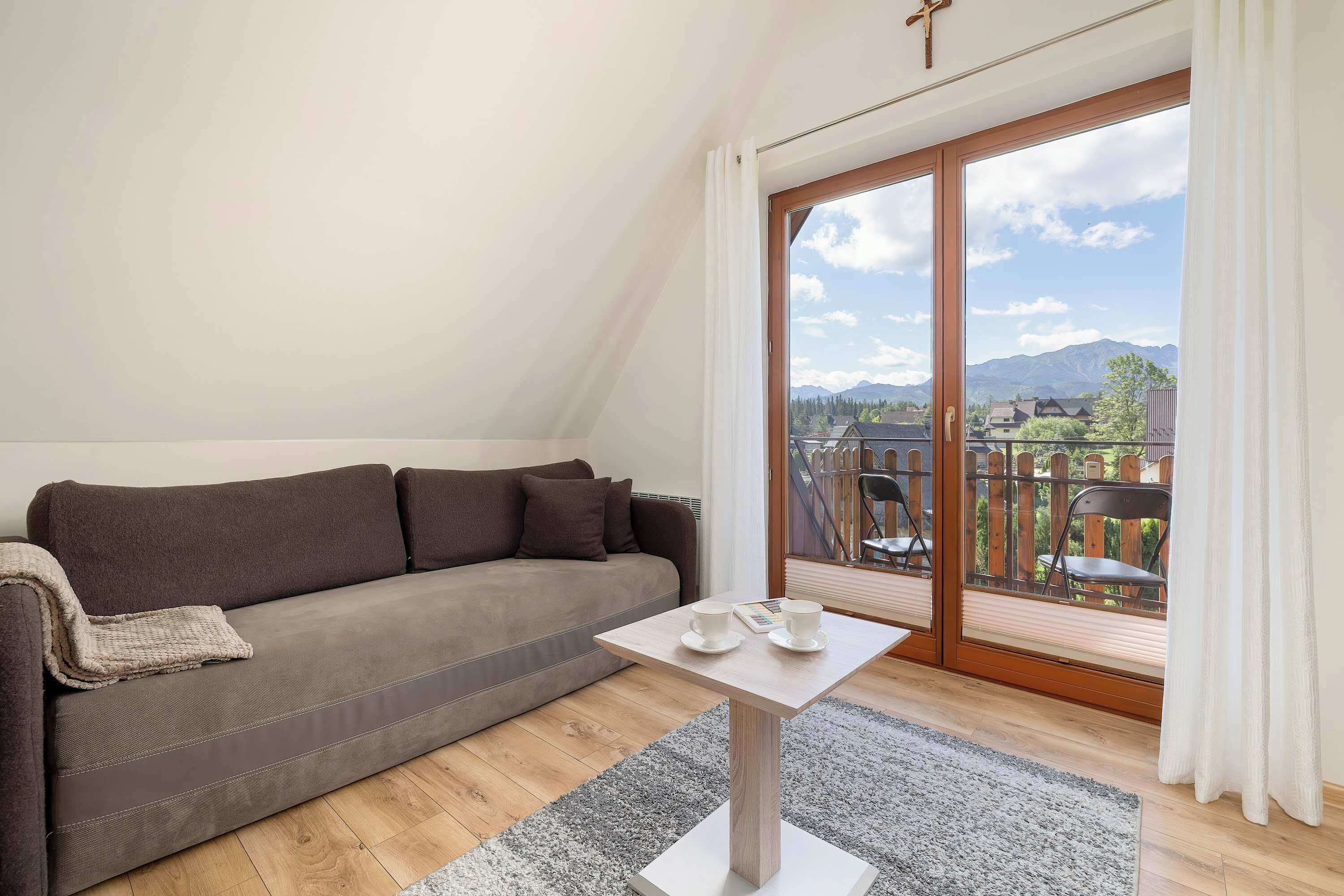A modern living room with a sofa, a small table, and a view of a town through large windows.