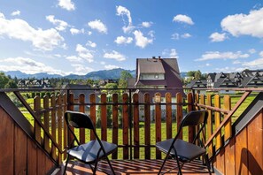 Terraza de madera con dos sillas, con vista a un paisaje montañoso y cielo despejado.