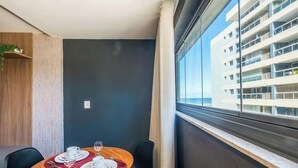 A hotel room with a dining table set for two, a window with a view of a building, and a plant on a shelf. - Studio in a Cond. With a Pool Near the sea Aru0123 (Salvador)